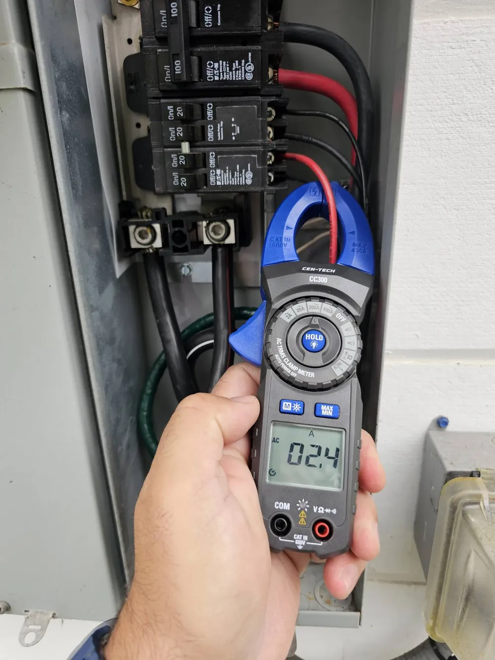 Juan de la Cruz taking an amperage reading with a clamp meter on the solar circuit inside an open main electrical panel